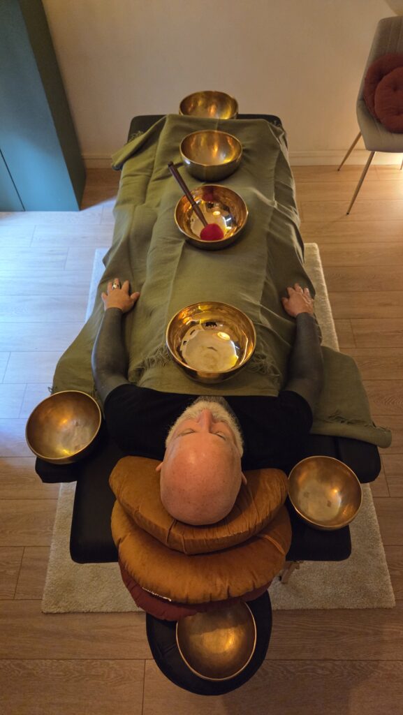 Une personne allongée sur la table de soins du Cabinet de Sonothérapie. Des Bols tibétains sont soigneusement disposés autours en préparation du soin.