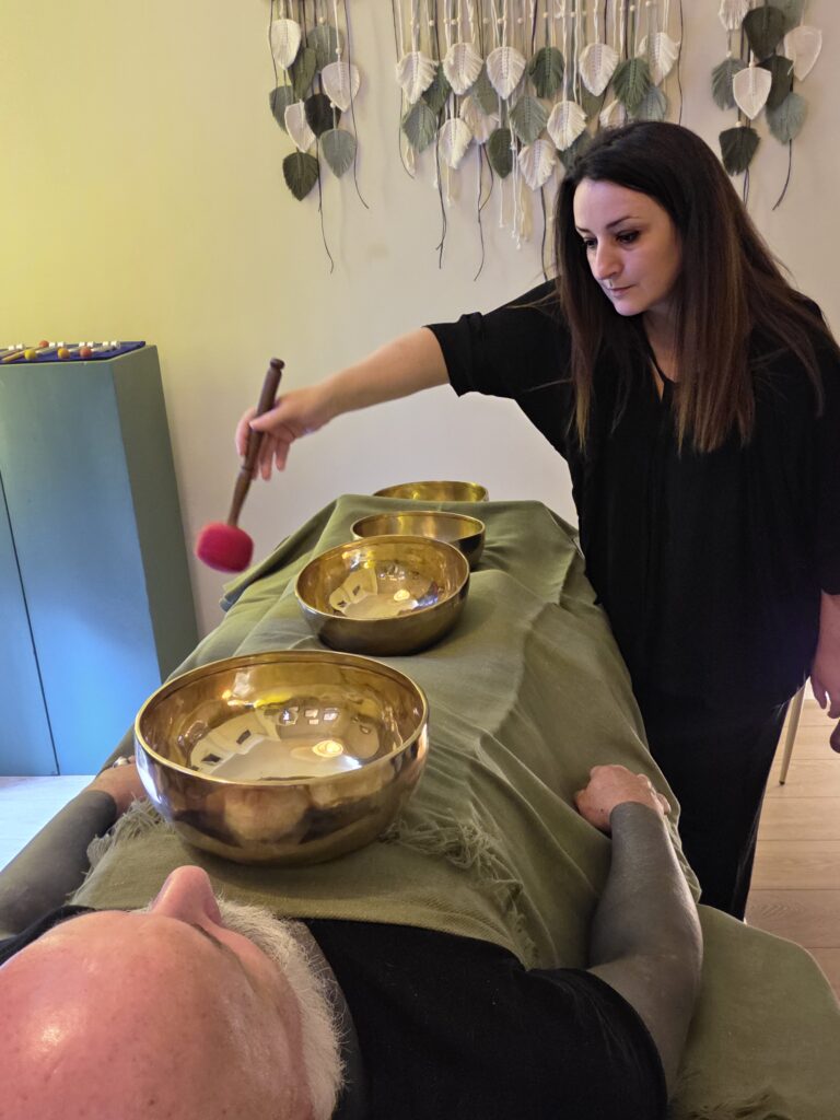 Une personne allongée sur la table de soins du Cabinet de Sonothérapie. Un soin avec des bols tibétains est en cours, réalisé par Aurélie Lastra de Natias.